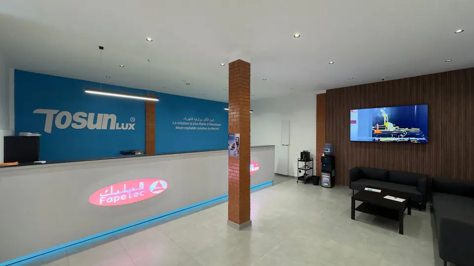 Comptoir d'accueil TOSUNLUX bleu, logo FAPELEC lumineux, coin salon avec canapés et écran.