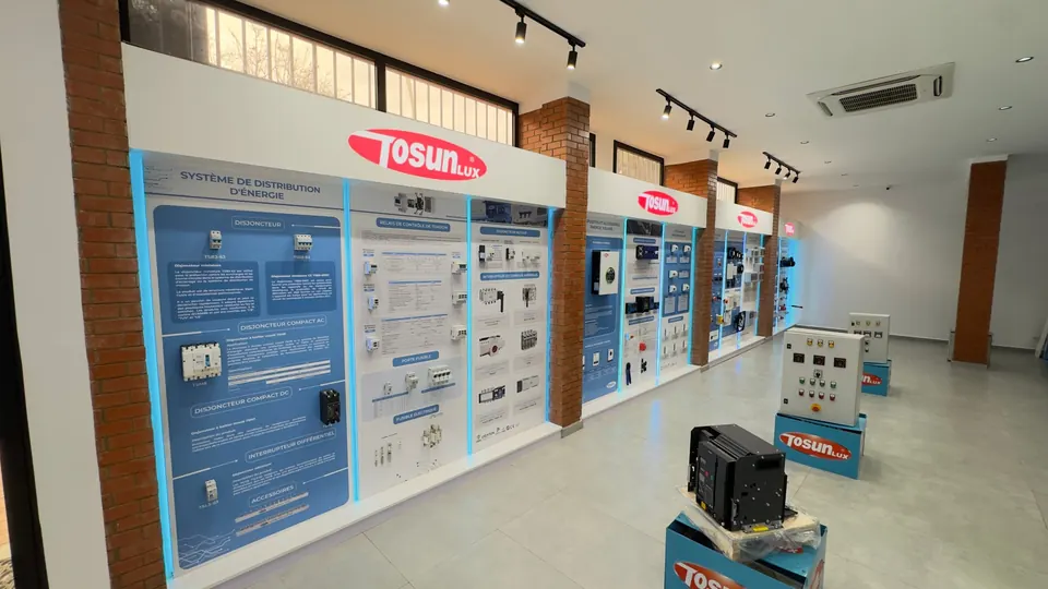 Vue d'ensemble du showroom : murs TOSUNLUX successifs, coffrets de commande câblés et disjoncteur de puissance sur socles TOSUNLUX.